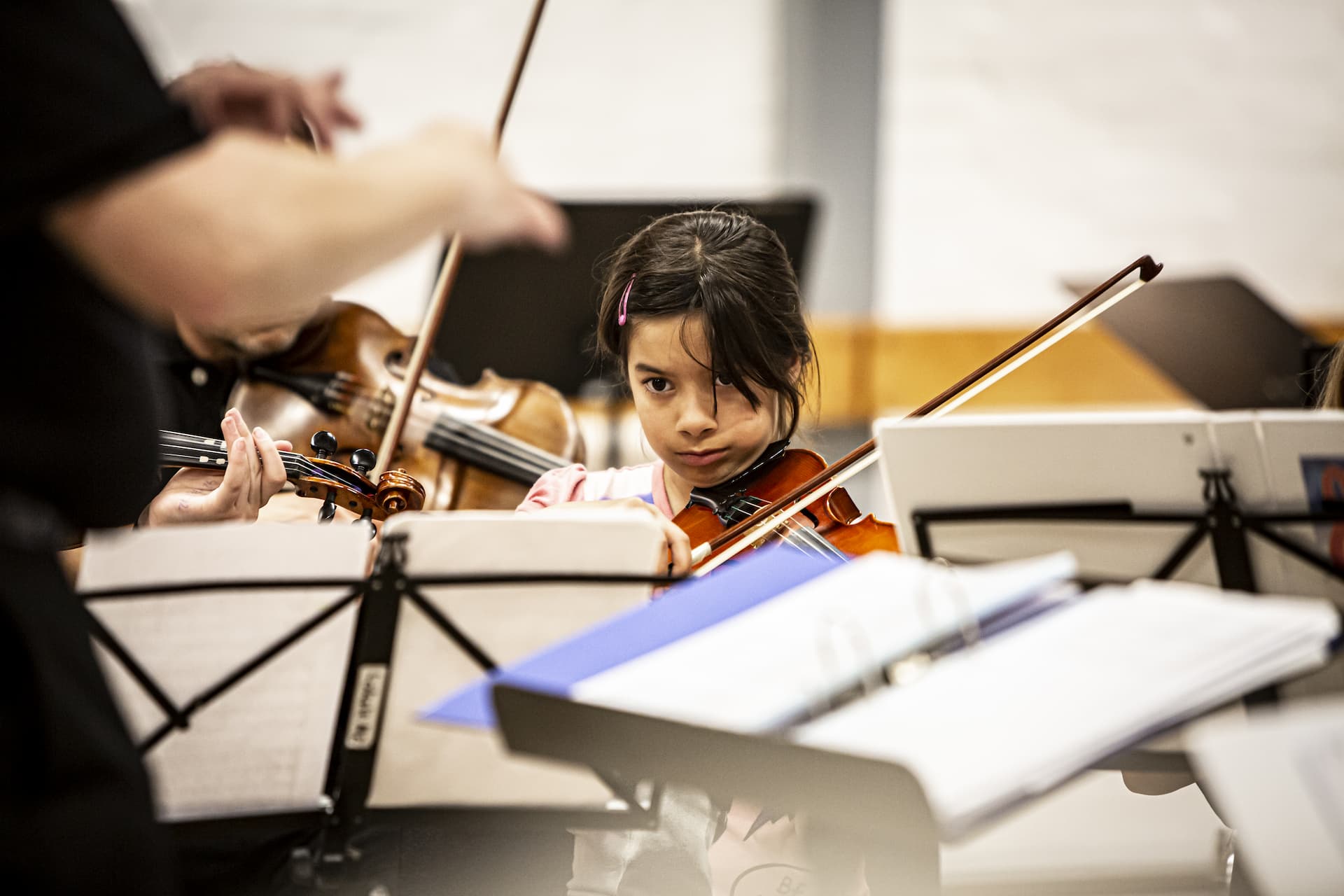 En lille pige spiller koncentreret violin, foran står en dirigent og dirigerer orkestret Minifresco