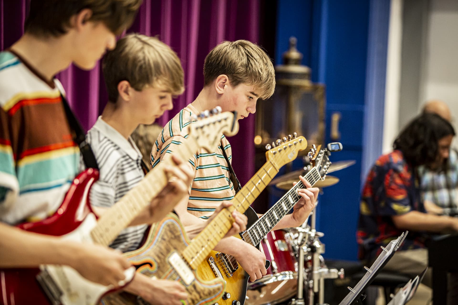 Tre drenge på stribe spiller el-guitar til skolekoncert