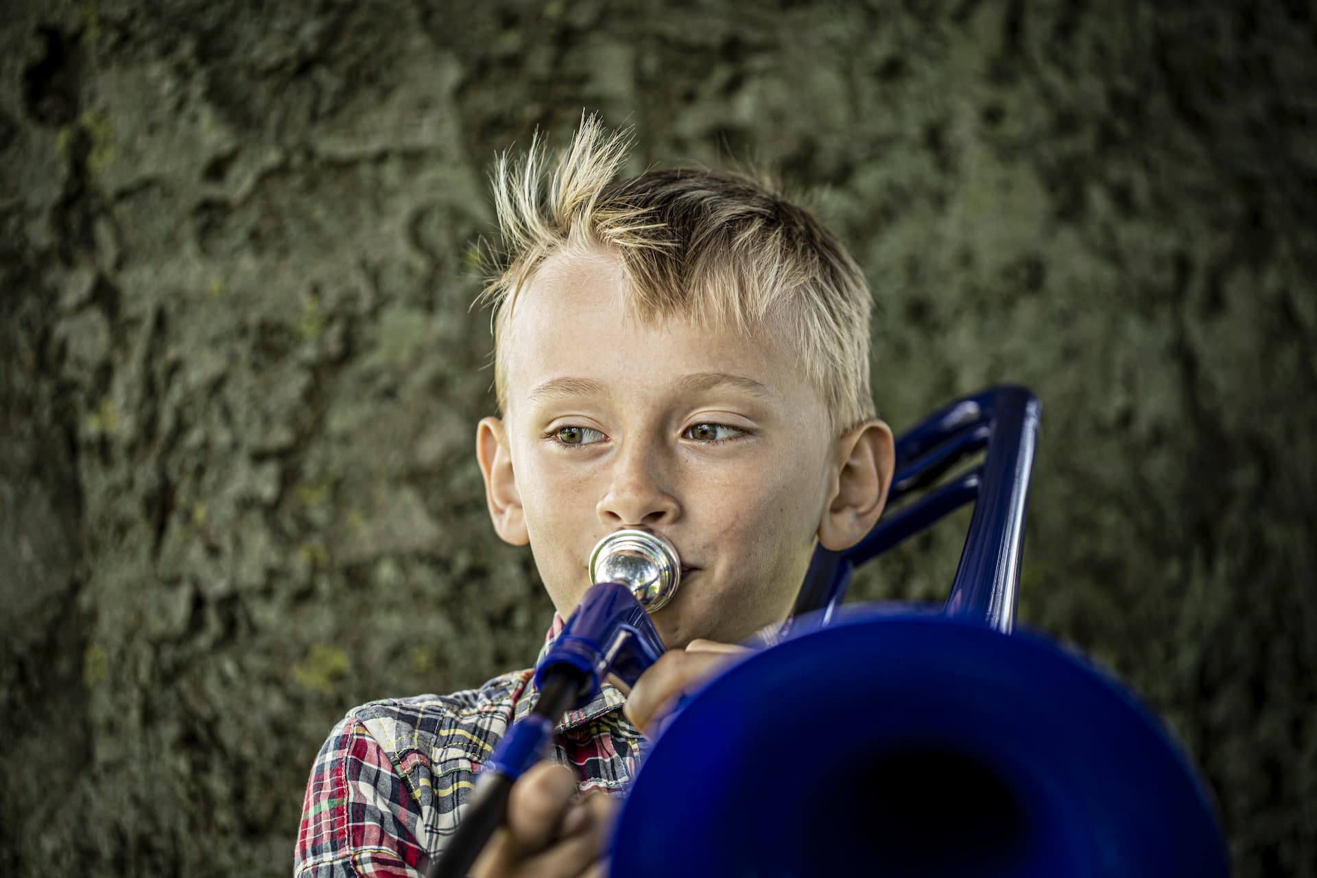 En dreng med strithår spiller på en blå trombone